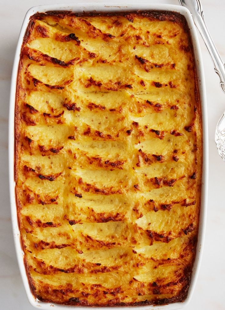 a casserole dish filled with potatoes on a white counter top next to two spoons