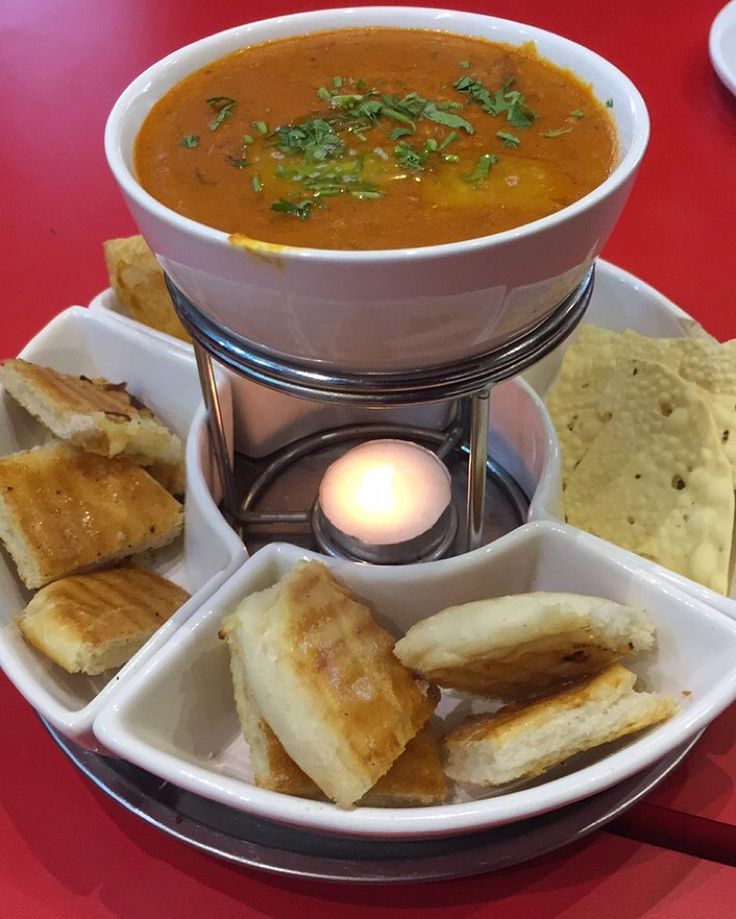 a bowl of soup, bread and chips on a plate with a lit candle in the middle