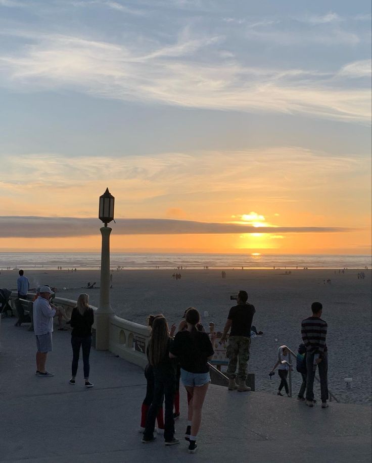 people are standing on the beach watching the sun go down