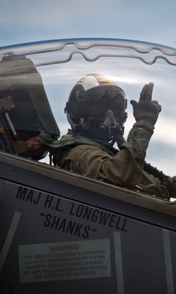 a man in a fighter jet flying through the air with his hand up to the sky