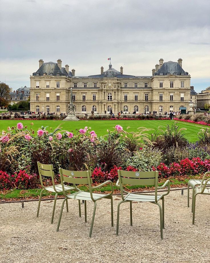 there are four chairs that are in front of a building with flowers on the ground