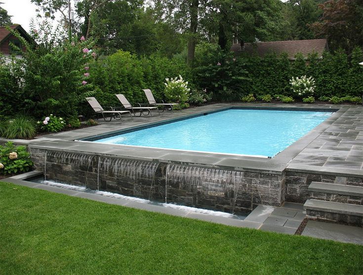 a backyard with a swimming pool surrounded by greenery and lawn chairs on the side