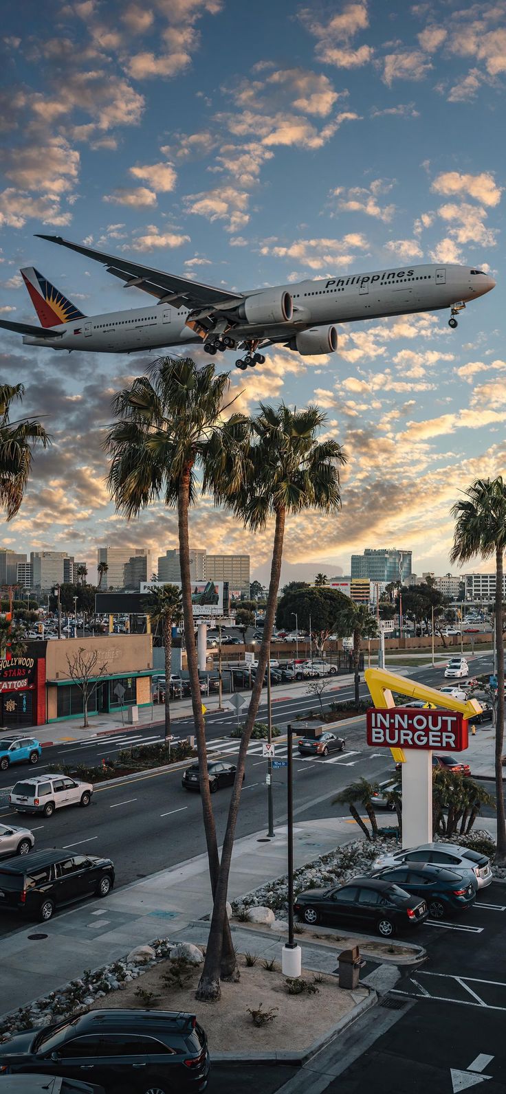 an airplane is flying low over a busy street with palm trees and buildings in the background