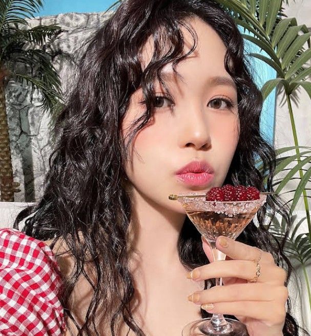 a woman holding a martini glass filled with raspberries in front of her face