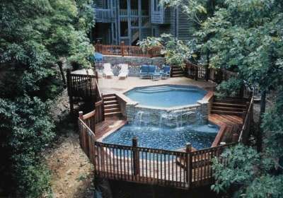 an above ground pool surrounded by trees and decking with a hot tub in the middle