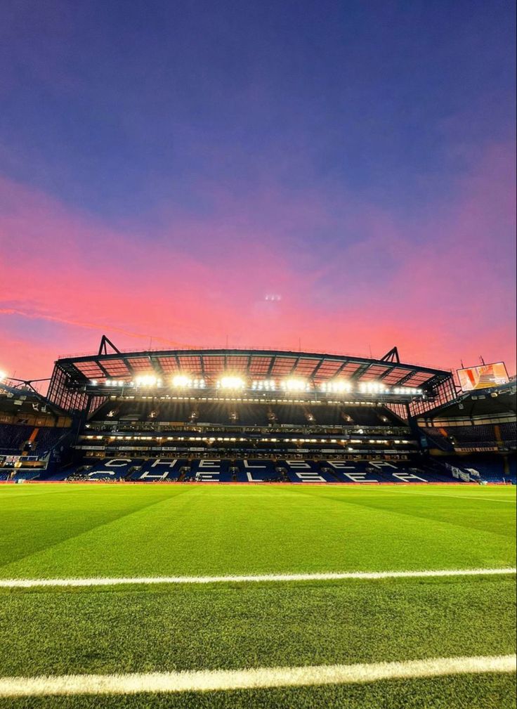 an empty soccer field at night with bright lights on the stands and grass in front of it