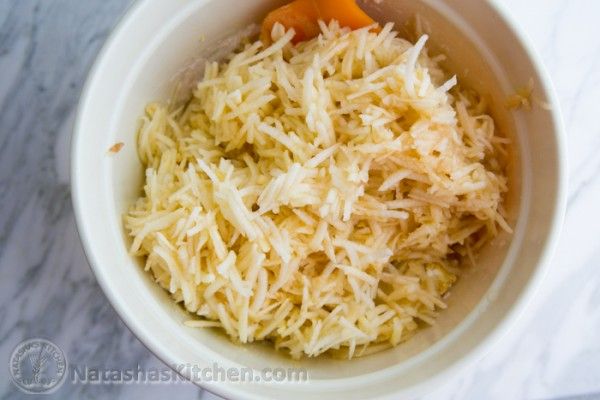 a white bowl filled with shredded cheese on top of a marble counter next to an orange spoon