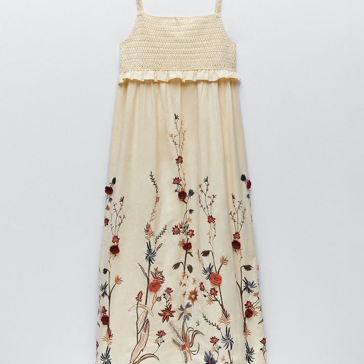 a white dress with flowers and birds on the front is hanging from a hanger