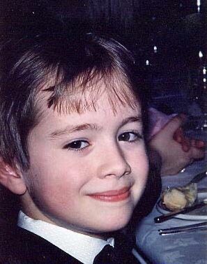 a young boy wearing a suit and tie at a dinner table with food on it