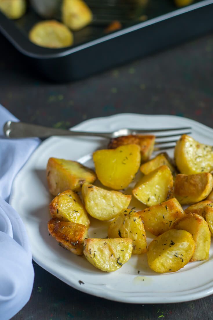 a white plate topped with potatoes on top of a table next to a fork and pan