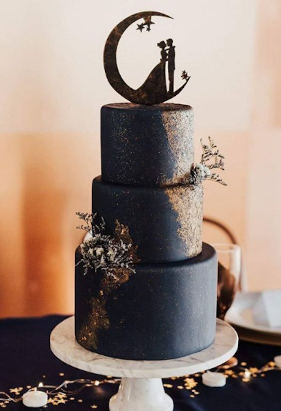 a wedding cake with a cat and moon decoration on the top, sitting on a table