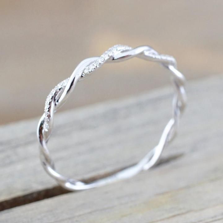 a white gold wedding band with twisted design on it, sitting on top of a wooden table