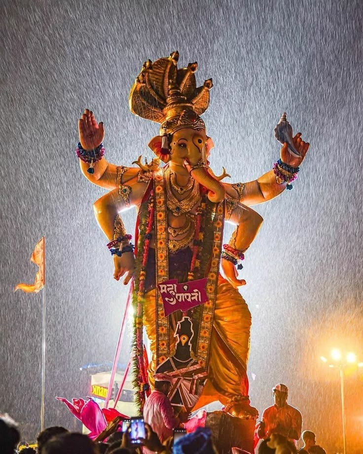 an idol is displayed in the middle of a crowd at night with rain falling down on it