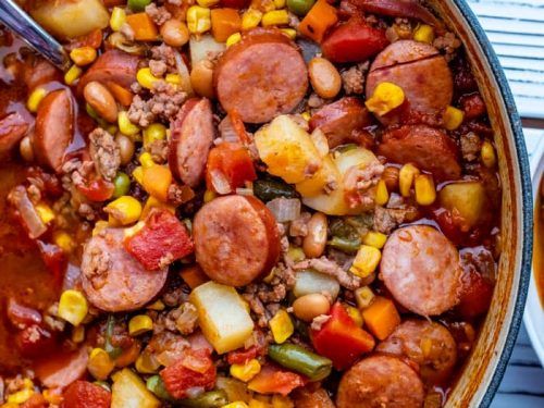 a large pot filled with sausage, potatoes and corn on top of a wooden table