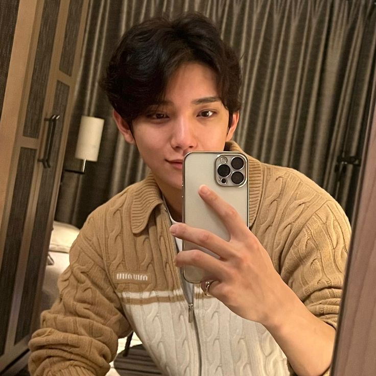 a young man taking a selfie in front of a mirror with his cell phone