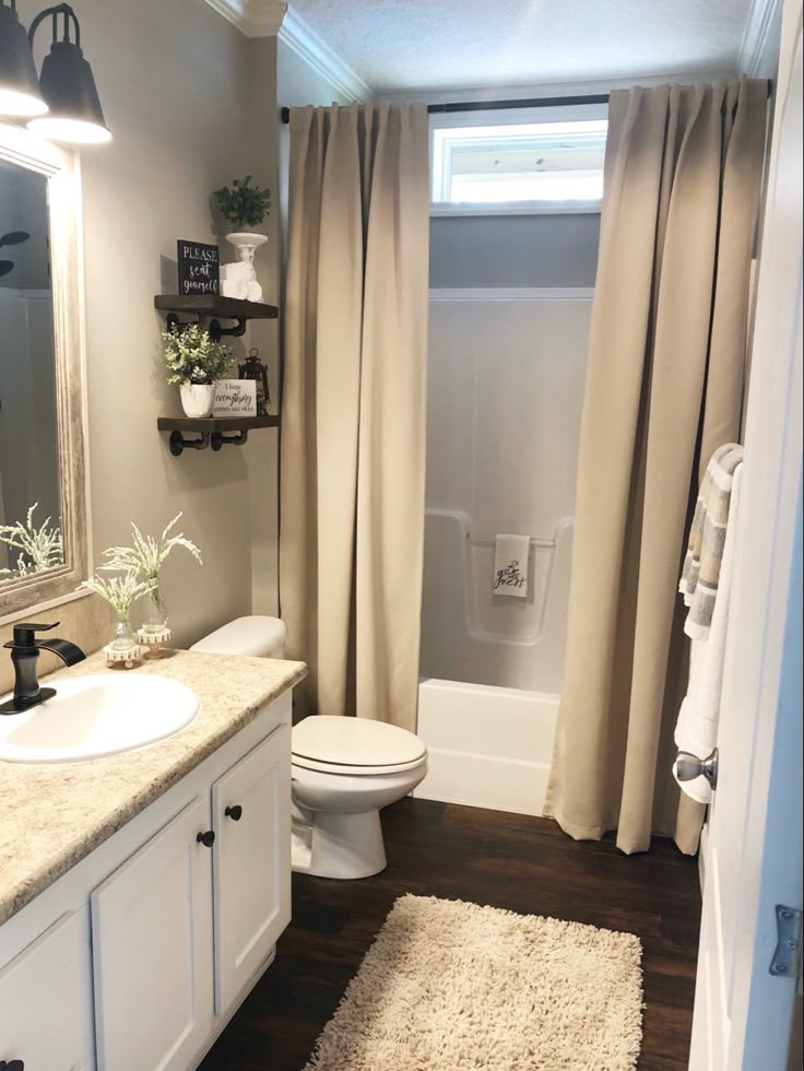 a bathroom with a white toilet sitting next to a bath tub under a window covered in curtains