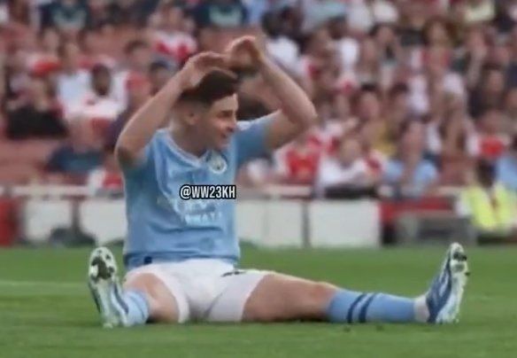 a soccer player sitting on the ground in front of a crowd with his hands behind his head