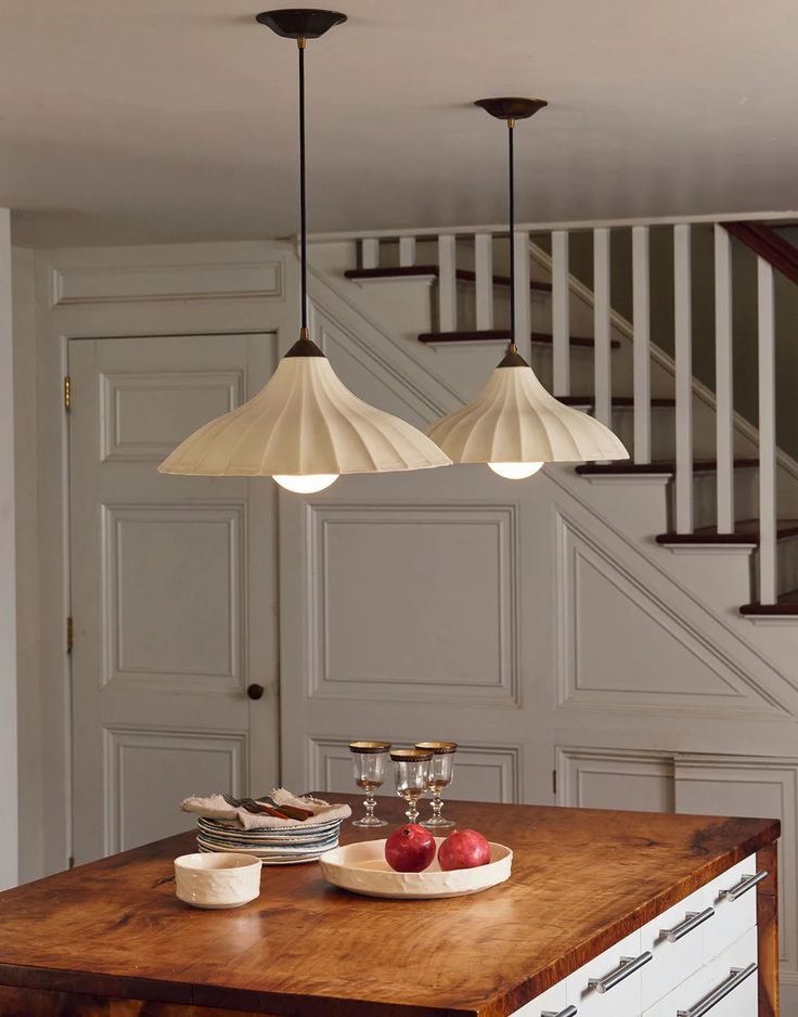 three lights hanging from the ceiling above a wooden table with plates and bowls on it