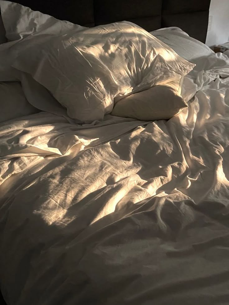 an unmade bed with white sheets and pillows