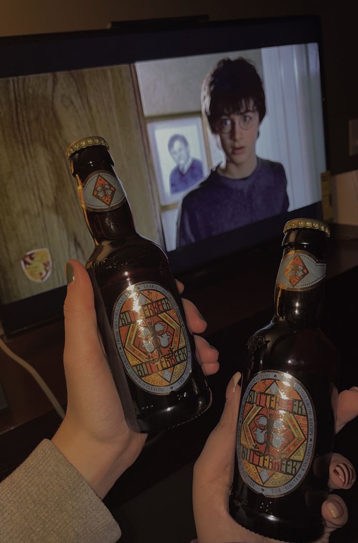 two people holding up beer bottles in front of a flat screen tv with the image of harry potter on it