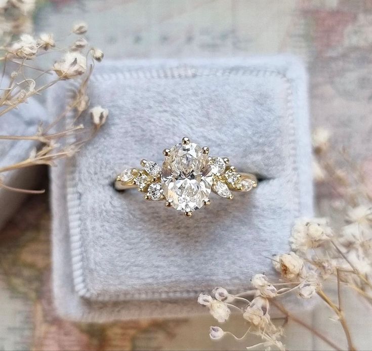 an engagement ring sitting on top of a white box next to dried plants and flowers