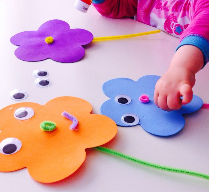 a child is playing with paper flowers and beads on the table, while another child holds their hand out to touch them