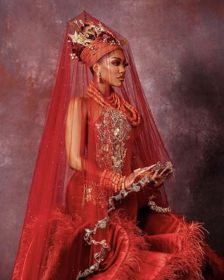 a woman in a red dress and veil with feathers on her head is holding a book