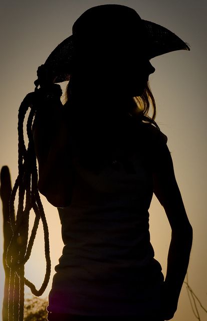 the silhouette of a woman wearing a cowboy hat and holding a long braid in her hand