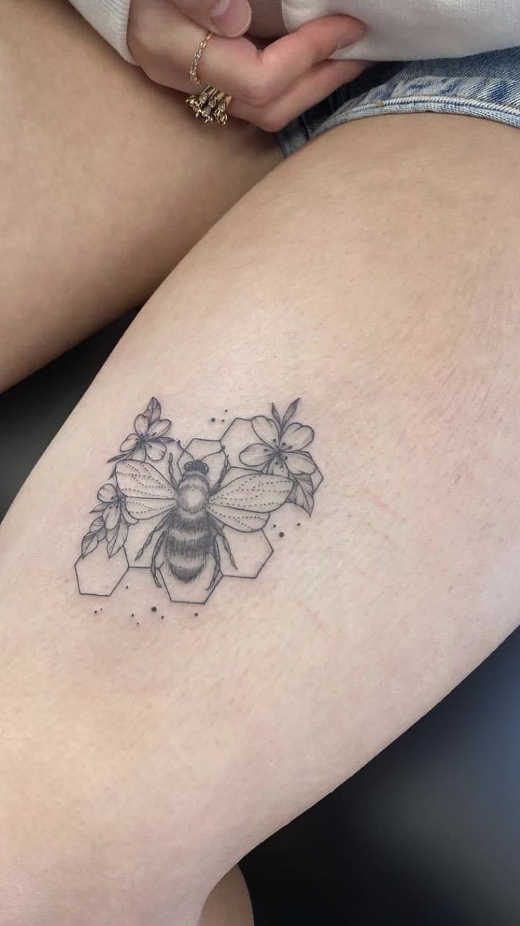 a woman's thigh with a tattoo of a bee and flowers on the side