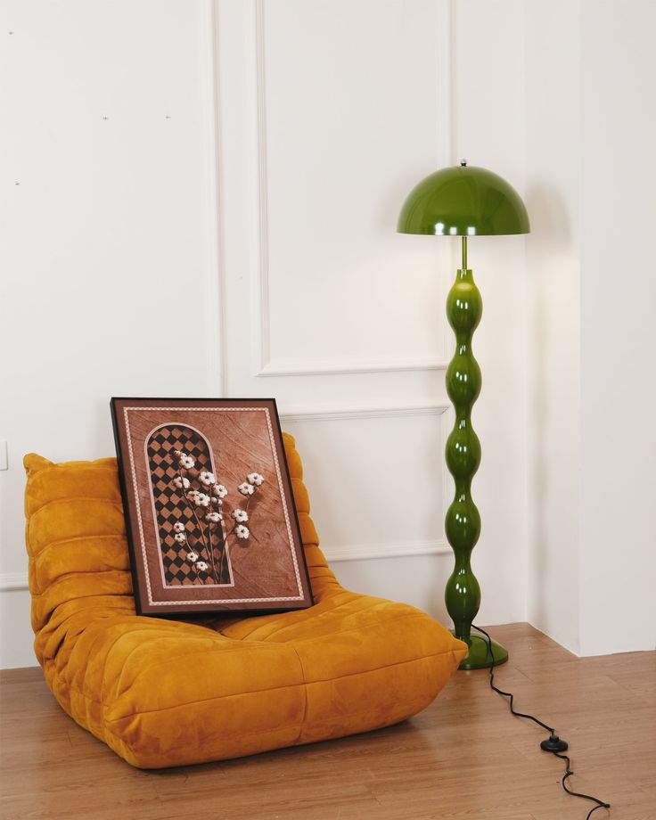 a green lamp sitting on top of a wooden floor next to a yellow chair and a painting