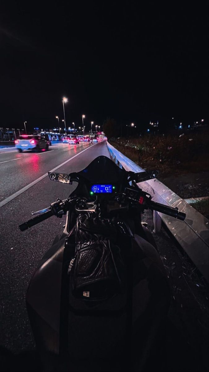 the motorcycle is parked on the side of the road at night with traffic behind it