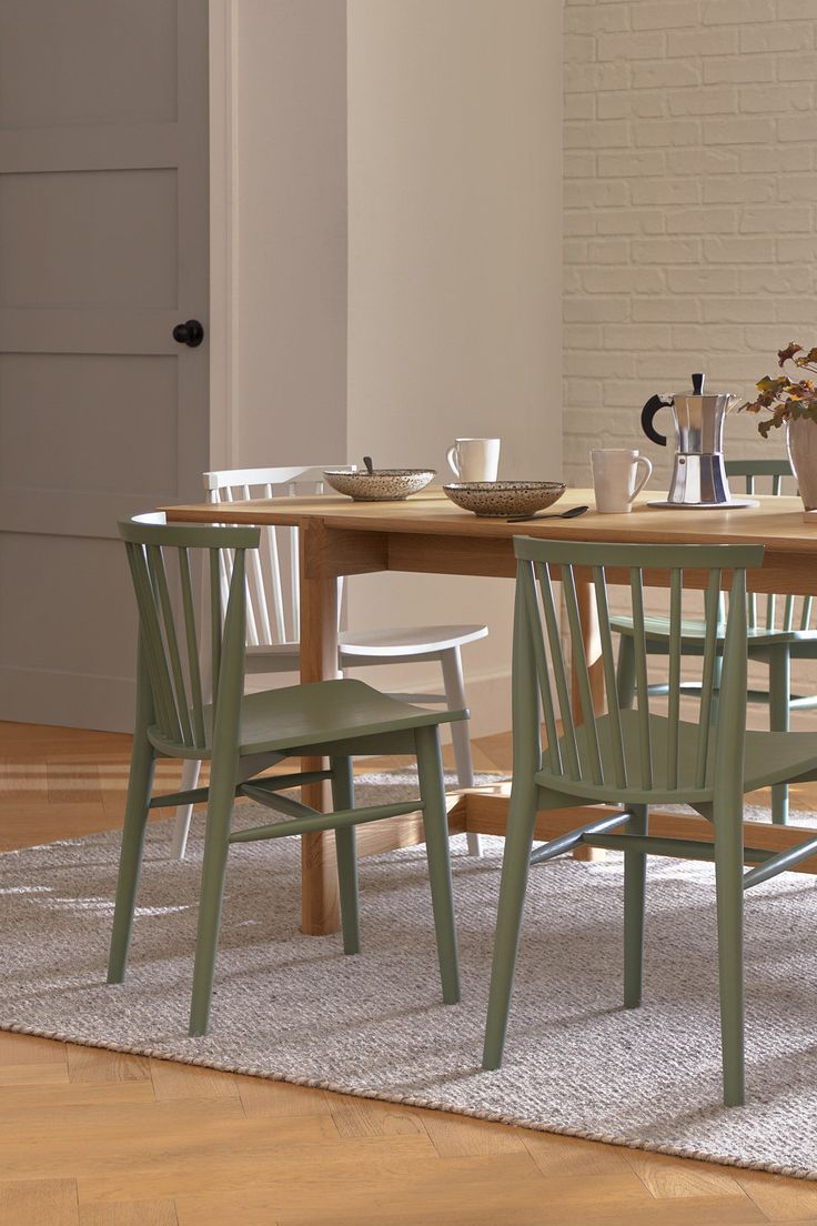 a wooden table with four chairs around it on a rug in front of a white brick wall