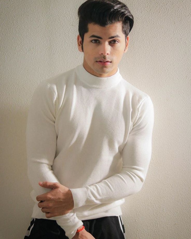 a man in white shirt and black pants standing next to a wall with his hands on his hips