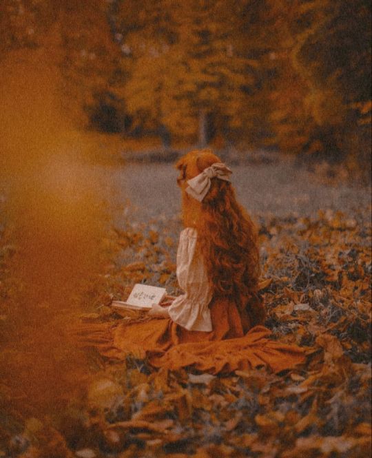 a teddy bear sitting on the ground with a book in its lap and wearing a face mask