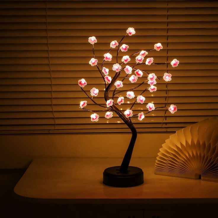 a lighted tree with pink flowers sitting on top of a table next to an open book