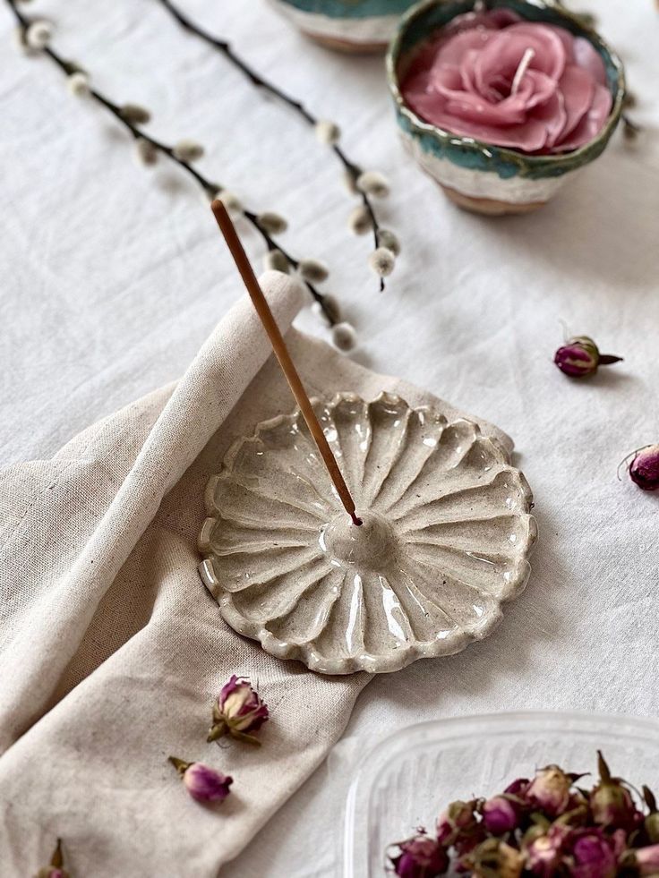 tea cups with flowers and sticks in them sitting on a white cloth covered tablecloth