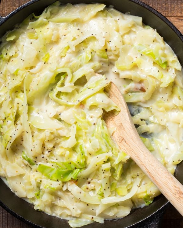 a skillet filled with pasta and broccoli on top of a wooden table