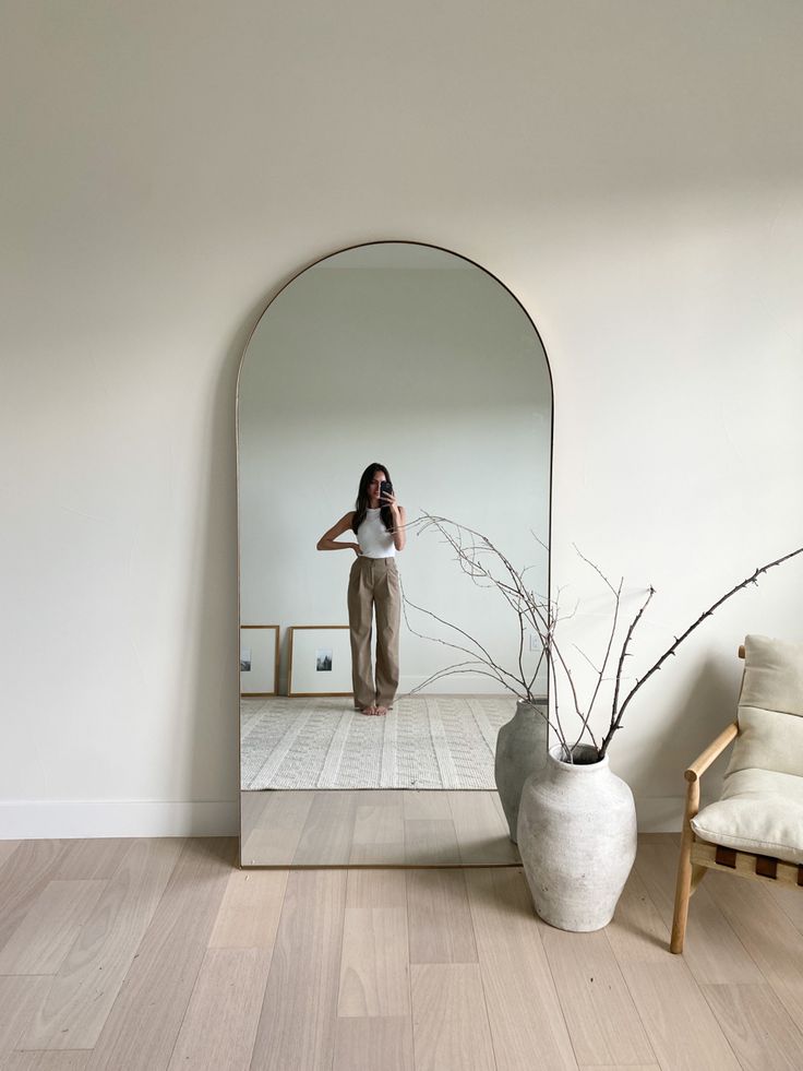 a woman taking a selfie in front of a mirror with a vase on the floor