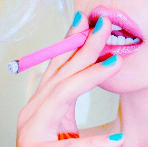 a woman with blue and pink nail polish holding a toothbrush up to her mouth