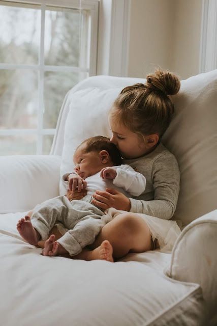 two young children are sitting on a white couch and one is holding the baby's head