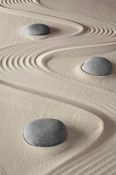 four rocks sitting on top of sand in the shape of spirals and circles with wavy lines