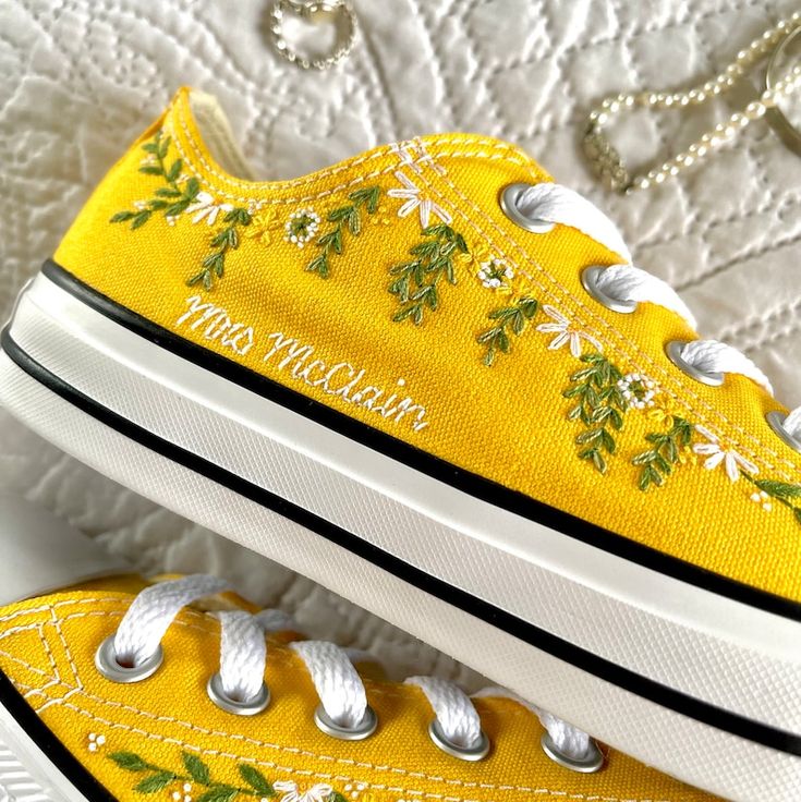 a pair of yellow shoes with flowers painted on the side and white laces around them