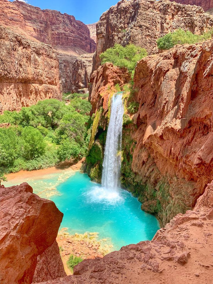 a waterfall in the middle of a canyon with blue water and green plants around it