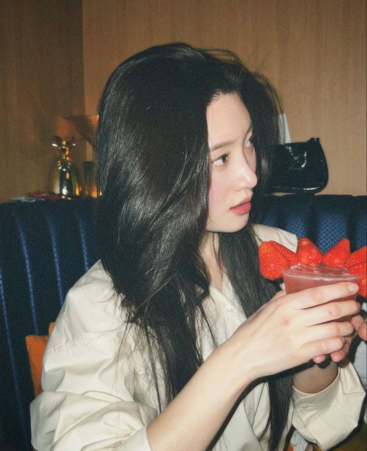 a woman sitting at a table with a drink and strawberries in front of her