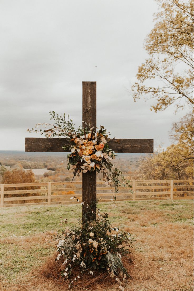 a cross decorated with flowers in the middle of a field