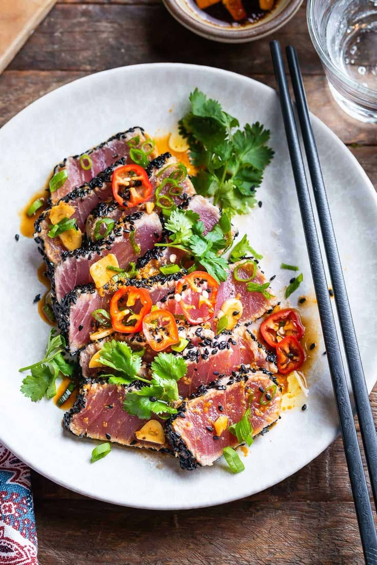 a white plate topped with meat and veggies next to chopsticks