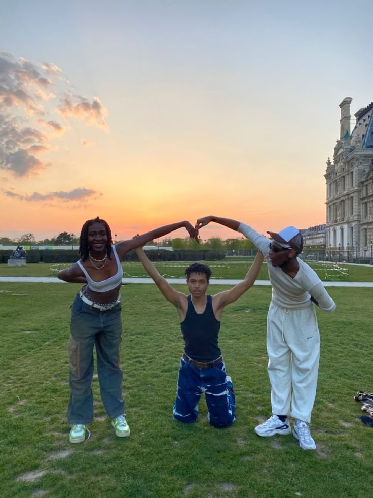 three people are standing in the grass with their arms up and one person is making a heart