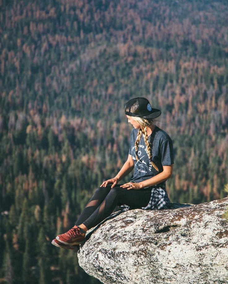 a young woman sitting on top of a rock next to a forest filled with trees