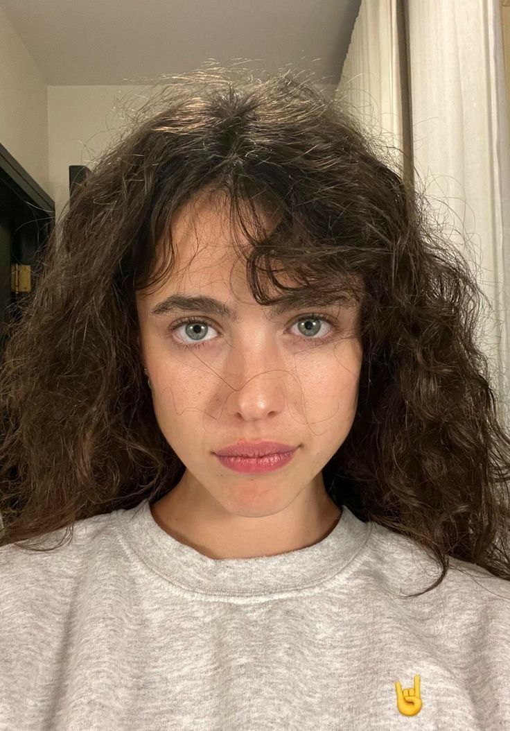 a young woman with curly hair and blue eyes is looking at the camera while wearing a grey sweatshirt