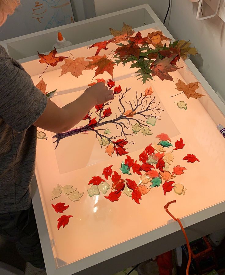 a young boy is working on an art project with autumn leaves and branches in the background